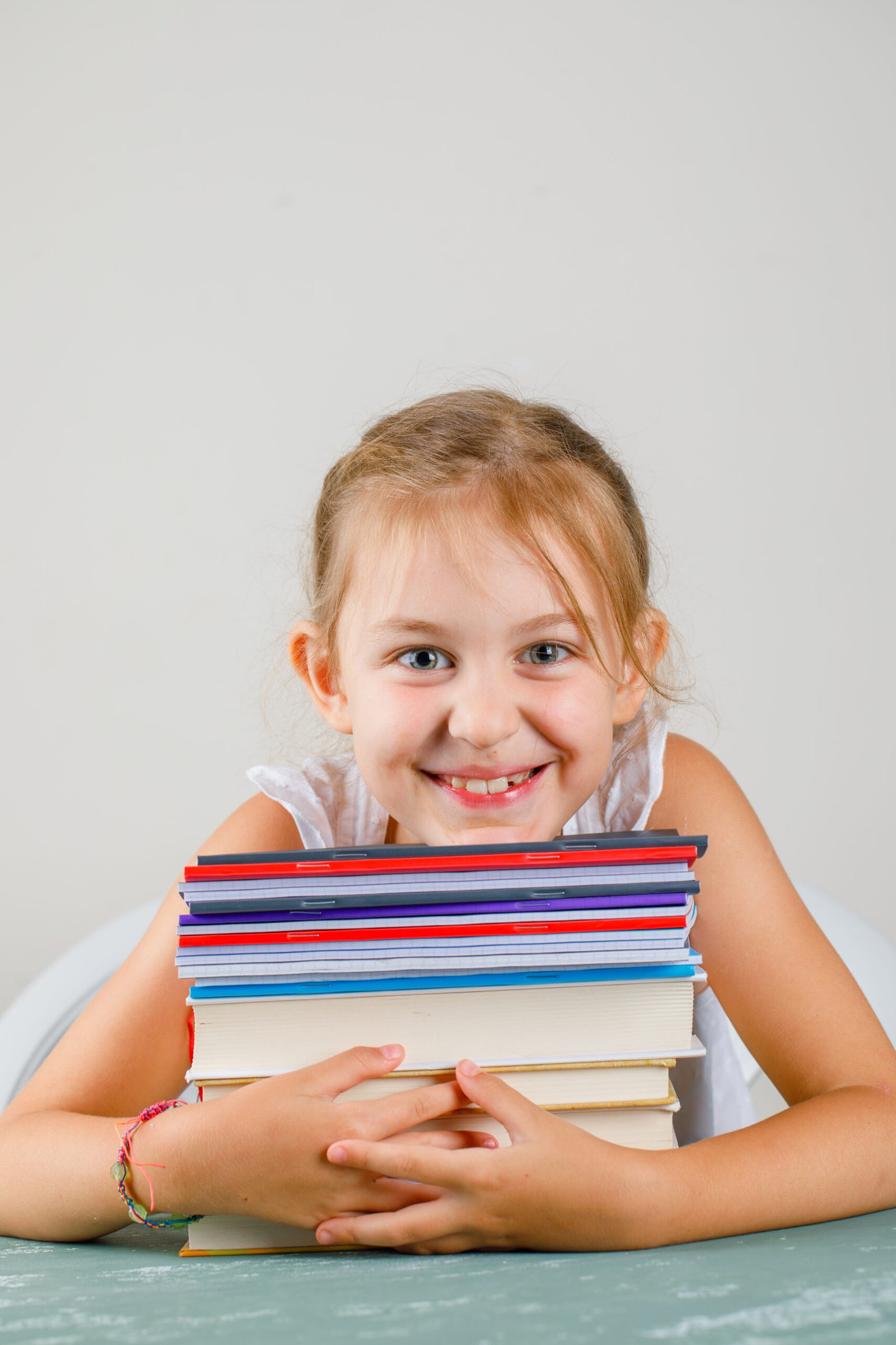 Back to school concept on plaster and grey background side view. little girl hugging copybooks and books.